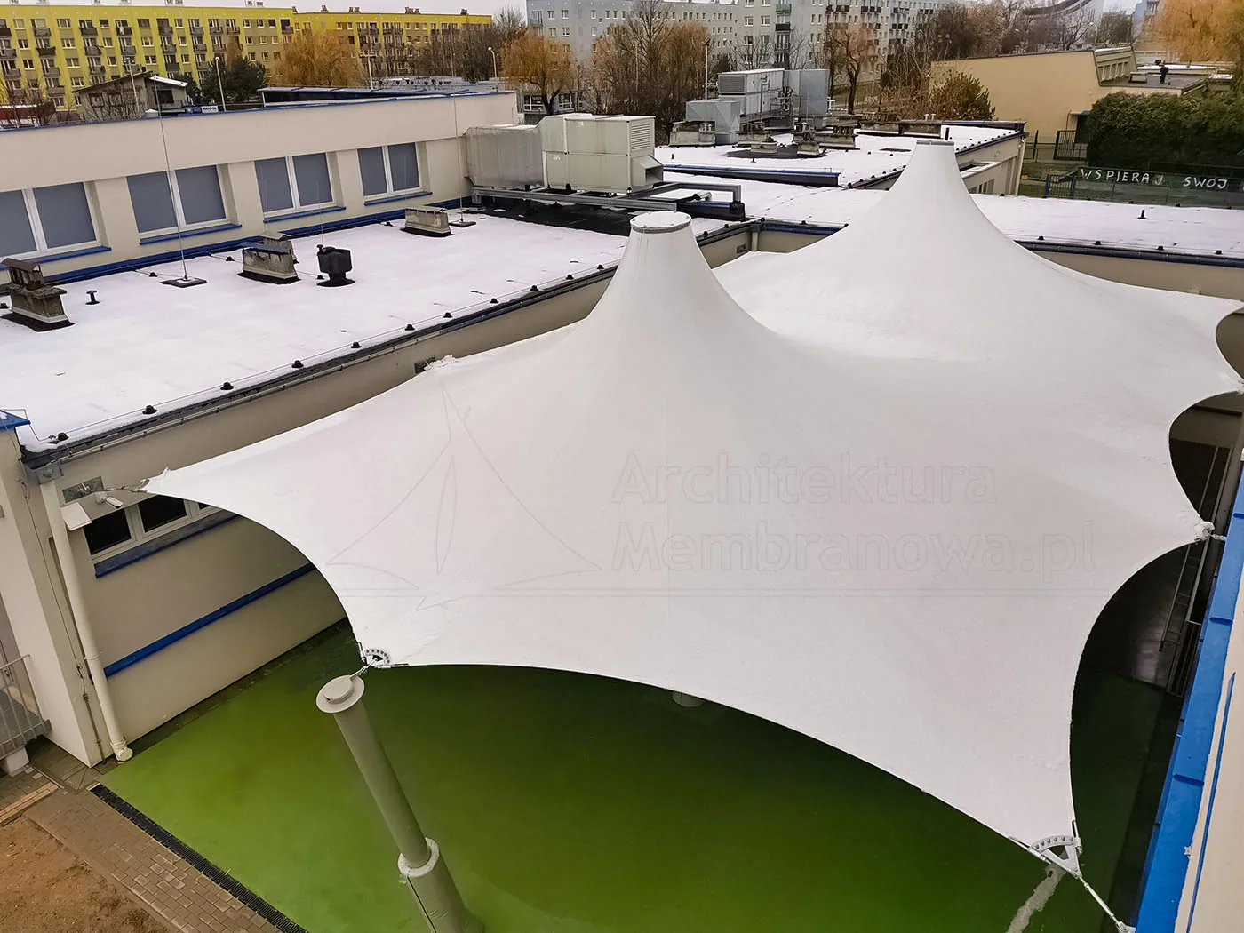 Białe dwustożkowe zadaszenie membranowe nad dziedzińcem placu zabaw, ujęcie z góry